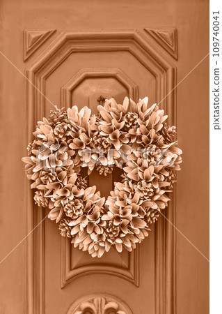Floral Christmas wreath crown hanging on entrance door of house, closeup. Toned in fashion blended pink-orange colour of year Peach Fuzz 109740041