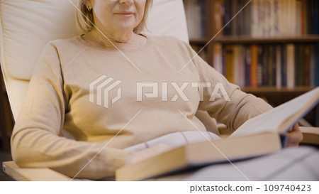 Close-up of a woman reading a book in her cozy study, a comfortable apartment, enjoying her hobby Close-up of a woman reading a book in her cozy study, a comfortable apartment, enjoying her hobby 109740423