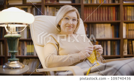 Portrait of a smiling mature woman knitting in the evening, entertainment, hobby Portrait of a smiling mature woman knitting in the evening, entertainment, hobby 109740436