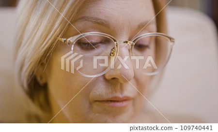 Close-up of the face of a concentrated blond woman in glasses, looking down, doing her hobby Close-up of the face of a concentrated blond woman in glasses, looking down, doing her hobby 109740441