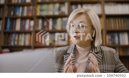 Serious woman talking over earbuds, conducting an online lesson in the library, busy teacher 109740502