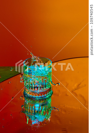 Ice cube falling down into glass with alcohol against orange background in neon light Ice cube falling down into glass with alcohol against orange background in neon light 109740545