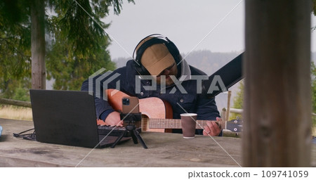 Male musician plays guitar, creates and records music outdoors Male musician plays guitar, creates and records music outdoors 109741059