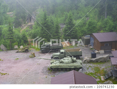 Military vehicles and a tank of the USSR army near buildings in the forest in the fog Military vehicles and a tank of the USSR army near buildings in the forest in the fog 109741230
