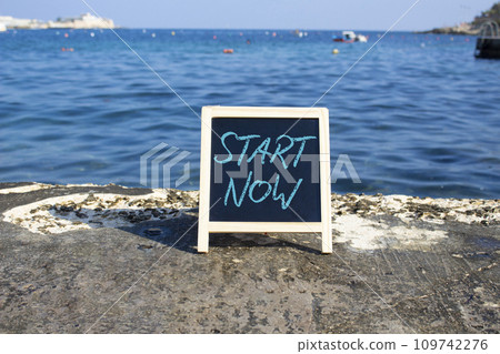 Start now symbol. Concept words Start Now on black chalk background. Beautiful sea background. Business and Start now concept. Copy space. Start now symbol. Concept words Start Now on black chalk background. Beautiful sea background. Business and Start now concept. Copy space. 109742276