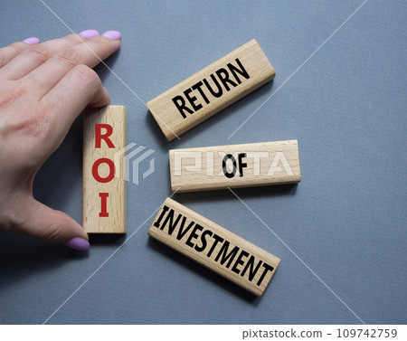 ROI - Return of Investment. Wooden cubes with words ROI. Businessman hand. Beautiful grey background. Business and ROI concept. Copy space. ROI - Return of Investment. Wooden cubes with words ROI. Businessman hand. Beautiful grey background. Business and ROI concept. Copy space. 109742759