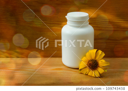 White bottle and yellow flower on a wooden background. Natural cosmetic product. Massage oil. Essential oil with herbal extract. White bottle and yellow flower on a wooden background. Natural cosmetic product. Massage oil. Essential oil with herbal extract. 109743438