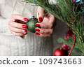 Female hands with red manicure and gold foil on the nails. Winter and Christmas time concept. Manicured woman's hands with Christmas decoration. 109743663