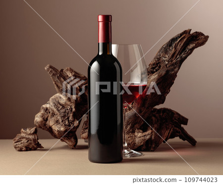 Bottle and glass of red wine with old weathered snag on a beige background. Bottle and glass of red wine with old weathered snag on a beige background. 109744023