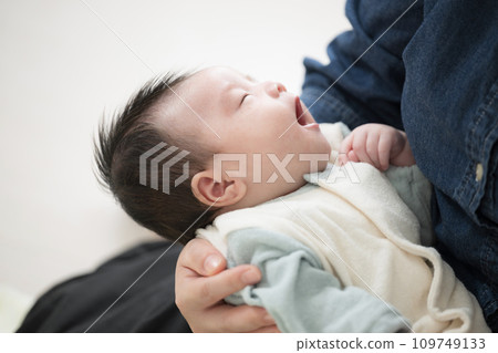 一個穿著嬰兒衣服的嬰兒被媽媽抱著打呵欠，上半身仰著的圖片 109749133
