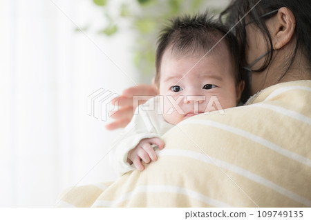 母親抱著穿著嬰兒衣服的嬰兒,拍拍他的背,鼓勵他打嗝。 母親抱著穿著嬰兒衣服的嬰兒,拍拍他的背,鼓勵他打嗝。 109749135