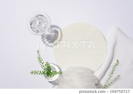 A round white podium is displayed with props on a white background. Ideal space for product display. Advertisements for shower gel, shampoo and other toiletries. 109750727