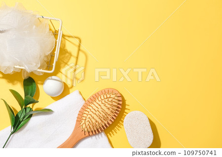 A bath sponge in an iron basket, green leaves, white ball, a towel, soap and a detangling comb are decorated in the left corner on a yellow background. Free space for product design and display. A bath sponge in an iron basket, green leaves, white ball, a towel, soap and a detangling comb are decorated in the left corner on a yellow background. Free space for product design and display. 109750741