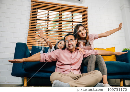 In their modern home an interracial family enjoys quality time together playing plane games with their daughter. Smiles laughter and togetherness fill the room with happiness. 109751170