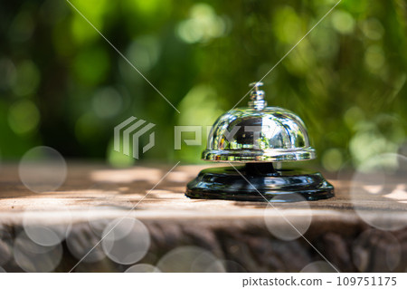 Hotel ring bell. Closeup of silver service restaurant bell on wooden counter desk, vintage bell to call staff outdoor in garden with green leaf 109751175