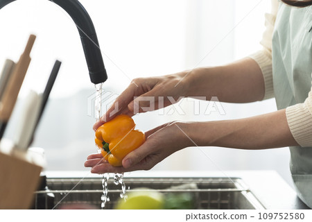 A woman in an apron washing paprika with water A woman in an apron washing paprika with water 109752580