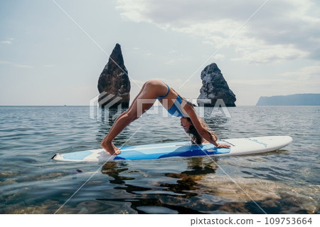 Woman sup yoga. Happy sporty woman practising yoga pilates on paddle sup surfboard. Female stretching doing workout on sea water. Modern individual female hipster outdoor summer sport activity. Woman sup yoga. Happy sporty woman practising yoga pilates on paddle sup surfboard. Female stretching doing workout on sea water. Modern individual female hipster outdoor summer sport activity. 109753664