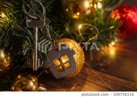 Gift key house with a keychain backdrop of Christmas tree. Building, design, project, moving to new house, mortgage, rent and purchase real estate. A gift for New Year, Christmas 109756318
