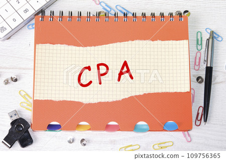 A CPA, a Certified public Accountant word is written on a sheet in a cage lying on a notebook on the table next to stationery A CPA, a Certified public Accountant word is written on a sheet in a cage lying on a notebook on the table next to stationery 109756365