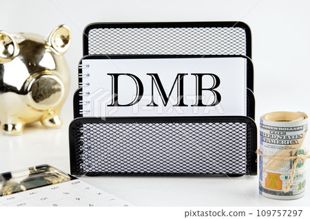 DMB text on a white piece of paper next to a piggy bank, a roll of money and a calculator on a white background 109757297