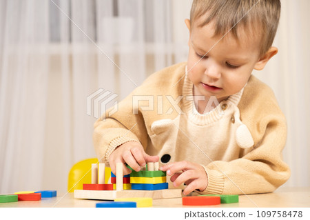 A two-year-old boy plays with wooden toys to develop logic and motor skills A two-year-old boy plays with wooden toys to develop logic and motor skills 109758478