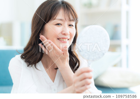 Middle-aged woman doing skin care in the living room Middle-aged woman doing skin care in the living room 109758586