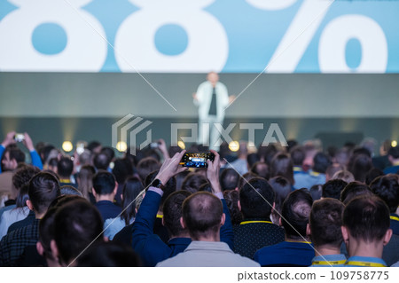 Back view of businesspeople listening to male speaker on stage during global presentation at conference hall  109758775