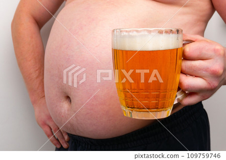 A pot-bellied man holds a mug of beer in his hand. Isolated on a white background. A pot-bellied man holds a mug of beer in his hand. Isolated on a white background. 109759746