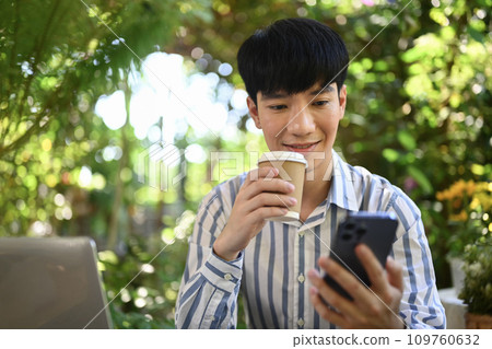 Handsome Asian man drinking coffee and using smartphone outside office building during break 109760632