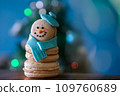 Snowman macaron dessert decorated with hat and scarf against Christmas tree, colorful lights and bokeh background. Merry Christmas and Happy New Year festive concept 109760689