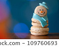 Snowman macaron dessert decorated with hat and scarf against colorful lights and bokeh background. Merry Christmas and Happy New Year festive concept 109760693