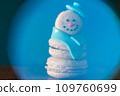 Snowman macaron dessert decorated with hat and scarf inside abstract blue snow globe. Merry Christmas and Happy New Year festive concept 109760699