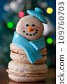 Snowman macaron dessert decorated with hat and scarf against colorful lights and bokeh background. Merry Christmas and Happy New Year festive concept 109760703