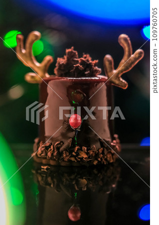 Chocolate reindeer cake with brown cream frosting decorated with antlers against colorful lights and bokeh background. Merry Christmas and Happy New Year festive concept Chocolate reindeer cake with brown cream frosting decorated with antlers against colorful lights and bokeh background. Merry Christmas and Happy New Year festive concept 109760705