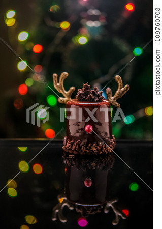 Chocolate reindeer cake with brown cream frosting decorated with antlers against colorful lights and bokeh background. Merry Christmas and Happy New Year festive concept Chocolate reindeer cake with brown cream frosting decorated with antlers against colorful lights and bokeh background. Merry Christmas and Happy New Year festive concept 109760708