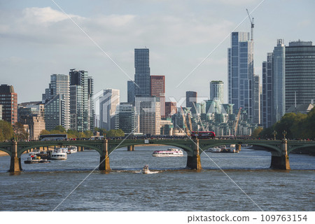 Distant view of vehicles on Westminster bridge. Boats moving on Thames river with modern buildings in background. Scenic urban beauty of capital city in London. 109763154