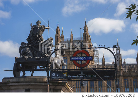 Low angle view of Boudiccan Rebellion statue and Westminster palace. Bronze sculpture infront of signboard at underground station with sky in background. Famous tourist attraction on sunny day. 109763208