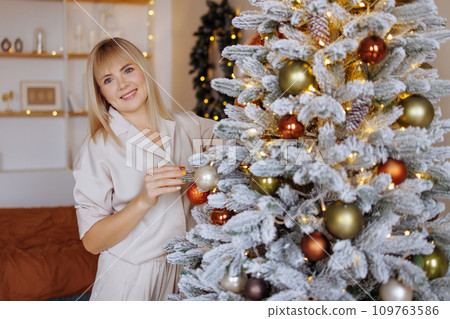 A woman decorates a Christmas tree. Side view. A woman decorates a Christmas tree. Side view. 109763586
