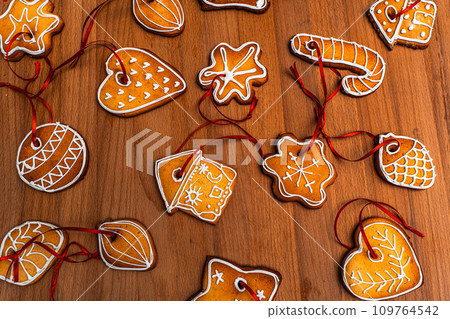 Wooden background with lots of gingerbread Christmas gingerbread in the shape of a house, heart. Deer. star, christmas tree toy, ball with white glaze. High quality photo 109764542