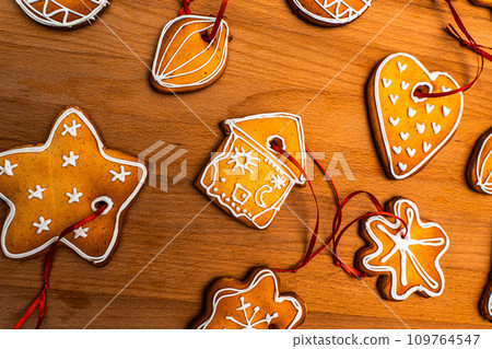 Wooden background with lots of gingerbread Christmas gingerbread in the shape of a house, heart. Deer. star, christmas tree toy, ball with white glaze. High quality photo 109764547