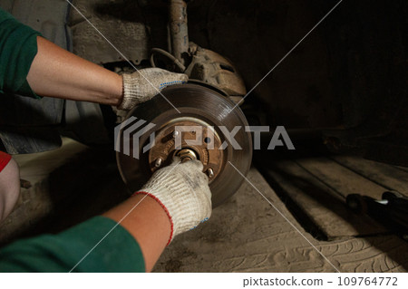 A man checks the hub of a car in a garage. A man is watching how to unscrew rusty bolts on a car hub. A man at home in the garage repairs a broken car. 109764772