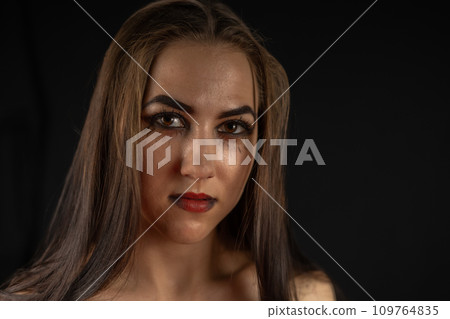 Halloween. Portrait of a beautiful woman in the style of a gothic witch on a black background. On Halloween, the witch stands in the dark and stares into the camera. Halloween holiday concept. 109764835