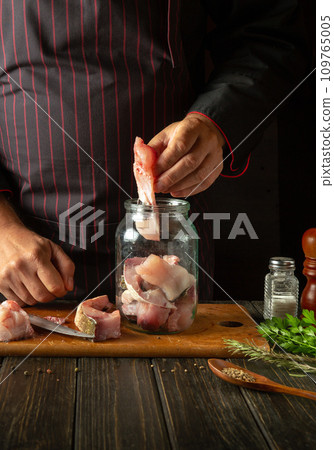 The chef prepares herring in the kitchen from fish steaks and aromatic spices. Canning fish in a jar with salt and coriander. The chef prepares herring in the kitchen from fish steaks and aromatic spices. Canning fish in a jar with salt and coriander. 109765005