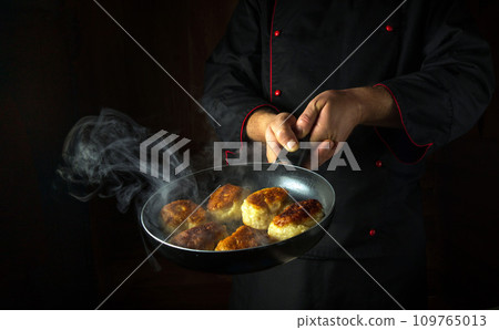 The chef fries donuts in a frying pan. The concept of preparing a Polish national dish in a restaurant kitchen. Black space for recipe or menu The chef fries donuts in a frying pan. The concept of preparing a Polish national dish in a restaurant kitchen. Black space for recipe or menu 109765013