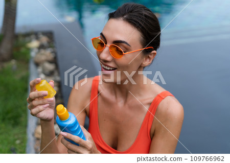 Beautiful european woman close shot with sun protection bottle cream spray at swimming pool, getting tan, tanned, brown soft healthy skin Beautiful european woman close shot with sun protection bottle cream spray at swimming pool, getting tan, tanned, brown soft healthy skin 109766962