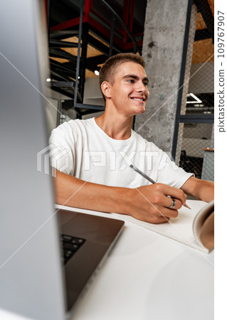 Young businessman making notes at tabletop with laptop in office 109767907