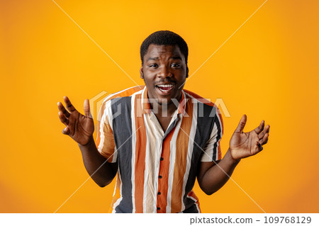 Surprised african stylish young man in striped shirt against yellow background 109768129