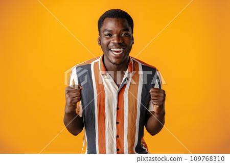 Happy excited young african man against yellow background Happy excited young african man against yellow background 109768310