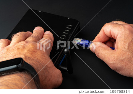 Man's hand plugging internet cable into wifi router Man's hand plugging internet cable into wifi router 109768814