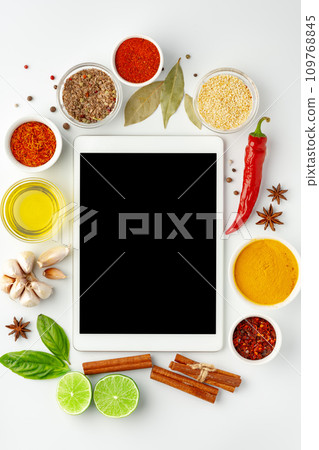 Digital tablet surrounded by cooking ingredients and spices on white background top view Digital tablet surrounded by cooking ingredients and spices on white background top view 109768845